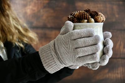 Midsection of woman holding coffee cup with pine cone at home