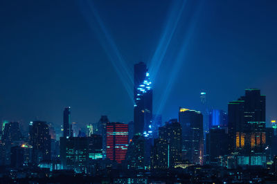 Illuminated buildings against blue sky at night