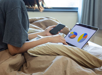 Midsection of woman using mobile phone while sitting on bed