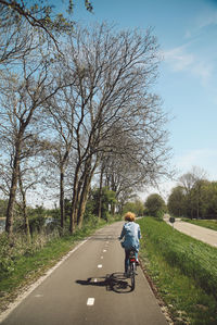 Rear view of woman riding bicycle on road against sky