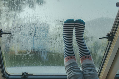 Low section of person seen through wet glass window