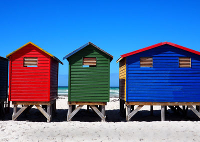 Wooden hut on beach against clear blue sky