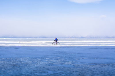 Man riding bicycle on snow covered land against sky