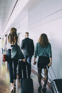 Full length rear view of multi-ethnic colleagues pulling luggage while walking at airport