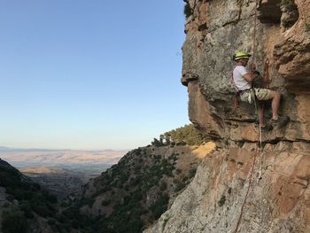 Man climbing on rock against clear sky