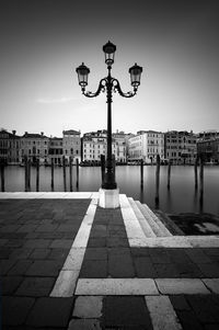 Street light on footpath by buildings against sky