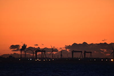 Silhouette built structure by sea against orange sky