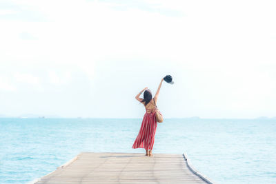 Rear view of woman standing at beach against sky