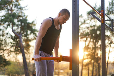 Side view of man exercising on gymnastics bar during sunset