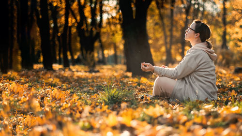 Caucasian middle aged woman meditating in lotus pose at autumn park with sunlight. yoga at fall