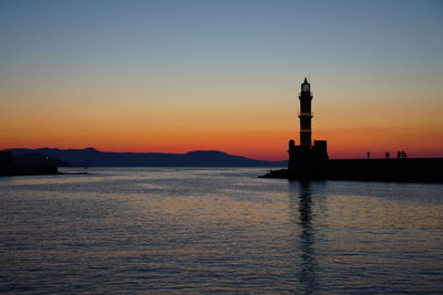 Silhouette lighthouse by sea against sky during sunset