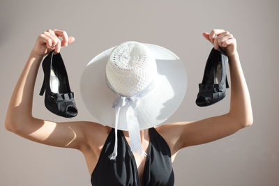 Midsection of woman holding hat while standing against white background