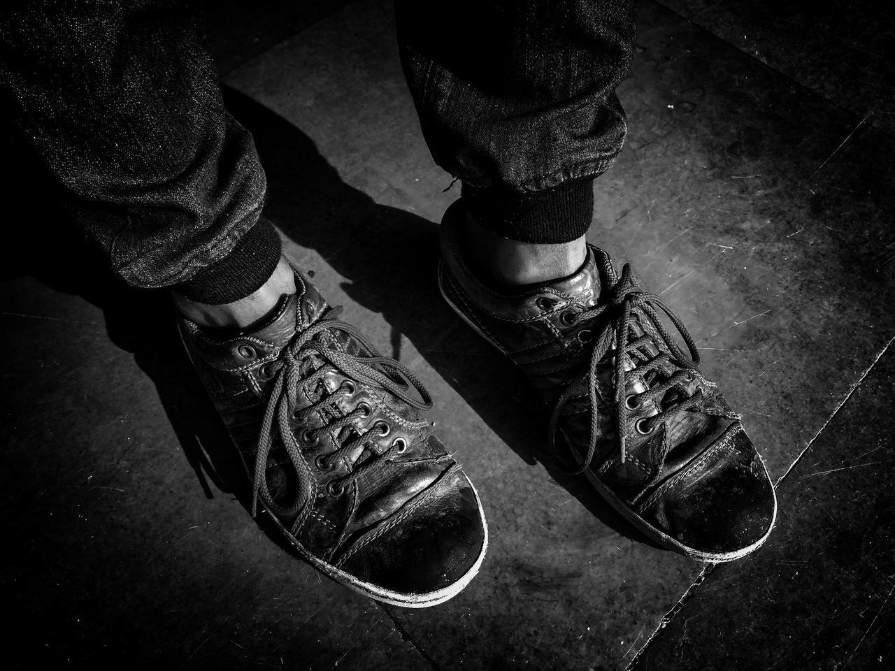 LOW SECTION OF MAN WEARING SHOES STANDING ON FLOORING