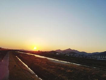 Road by agricultural field against clear sky during sunset