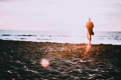 Rear view of man standing on beach against sky during sunset