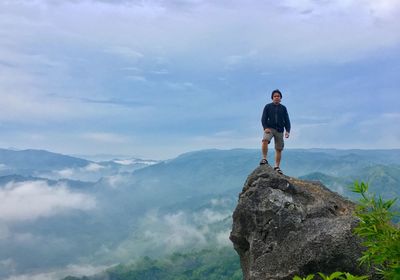 Full length portrait of hiker sitting on rock by mountains against cloudy sky