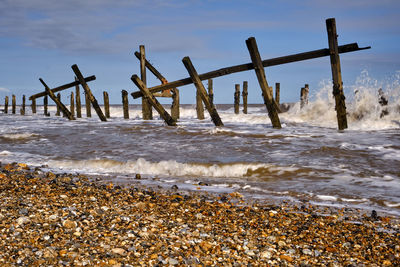 Wooden posts in sea against sky