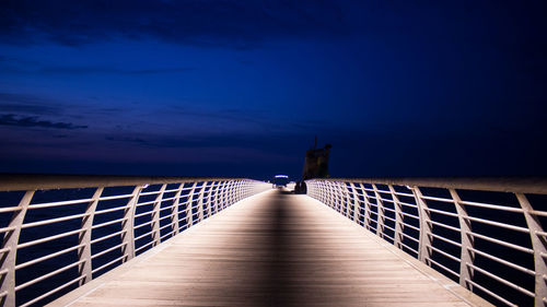 Jetty leading towards sea against sky at night