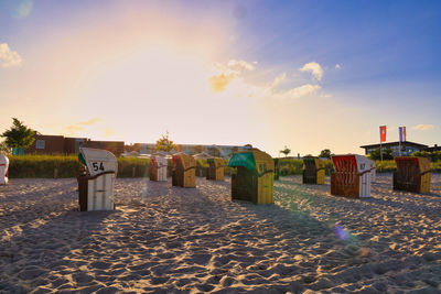 Hooded beach chairs against sky during sunset