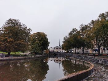Reflection of trees in canal against sky in city