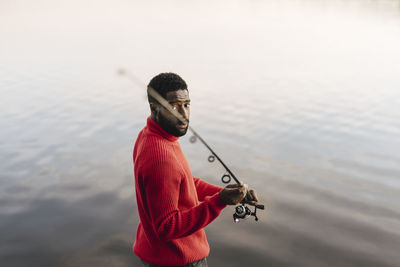 Man holding fishing rod at lakeshore during sunset