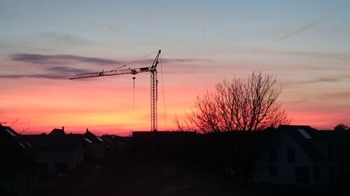 Silhouette cranes against sky at sunset