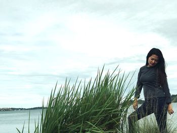 Young woman standing by lake against sky