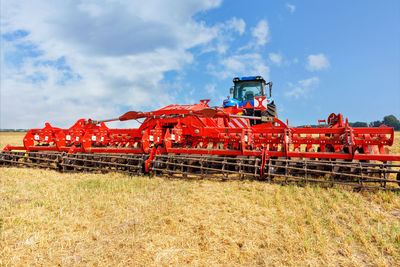 Universal red harrow as a hitch on an agricultural tractor against the background of   field.