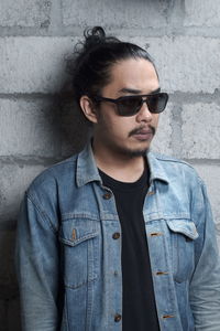 Young man looking away while standing against wall