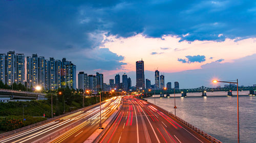 Light trails on road amidst buildings against sky at night