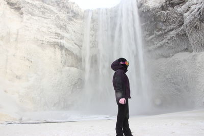 Side view of person wearing ski-wear against waterfall during winter