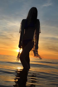 Woman standing on beach against sky during sunset