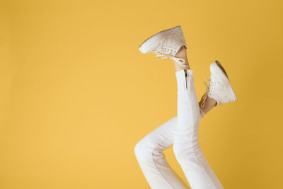 Low section of woman with umbrella against yellow background