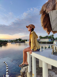 Rear view of woman standing against lake during sunset