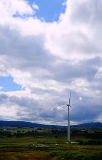 Wind turbines in field against cloudy sky