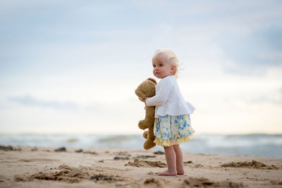 Girl with stuffed toy at beach against sky