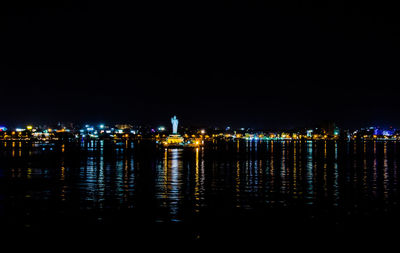 Illuminated cityscape by sea against sky at night