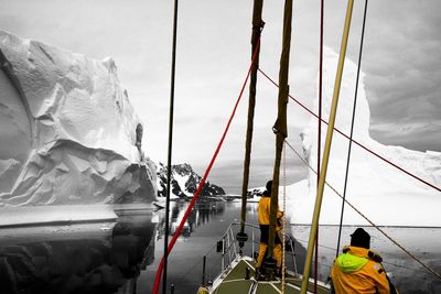 Rear view of people on sailboat by sea against sky