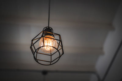 Close-up of illuminated light bulb hanging from ceiling