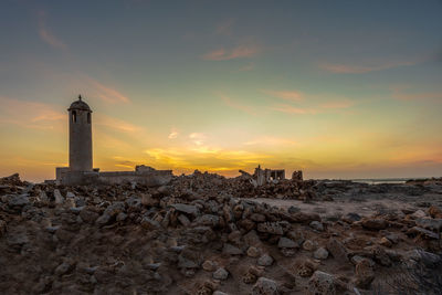 Lighthouse amidst buildings against sky during sunset