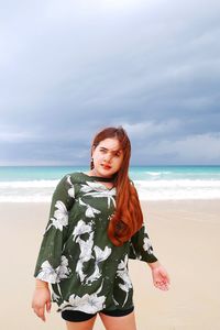 Young woman standing at beach against sky