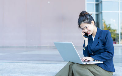 Woman using mobile phone while sitting on laptop