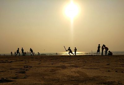 Silhouette people on beach against clear sky during sunset