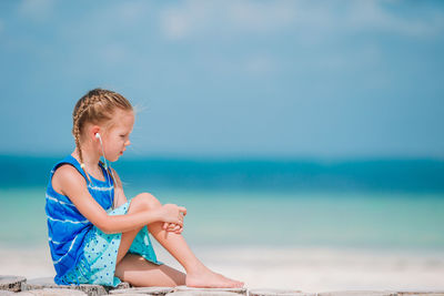 Side view of girl listening music sitting at beach