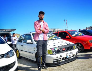 Portrait of man standing by car against blue sky