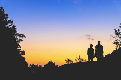 Silhouette people standing by trees against clear sky during sunset