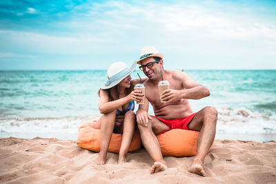 Friends sitting on shore at beach against sky