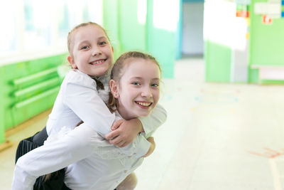 Portrait of girl piggybacking sibling while standing on floor