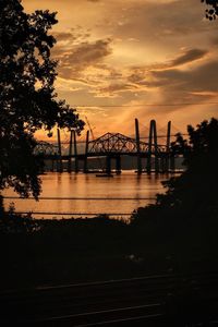 Silhouette bridge over river against sky during sunset