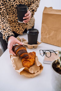 Woman at the workplace has a lunch of brown and chocolate croissants with coffee, food delivery